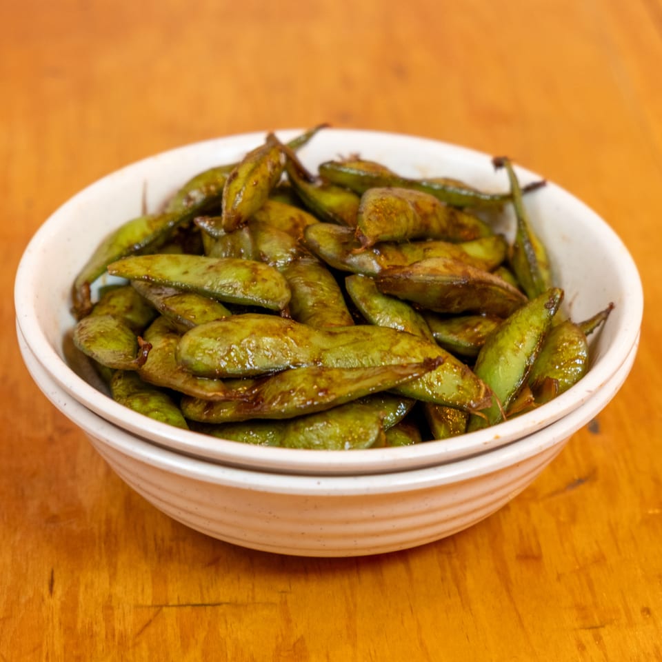 Bowl of sautéed green pods served on a wooden table.