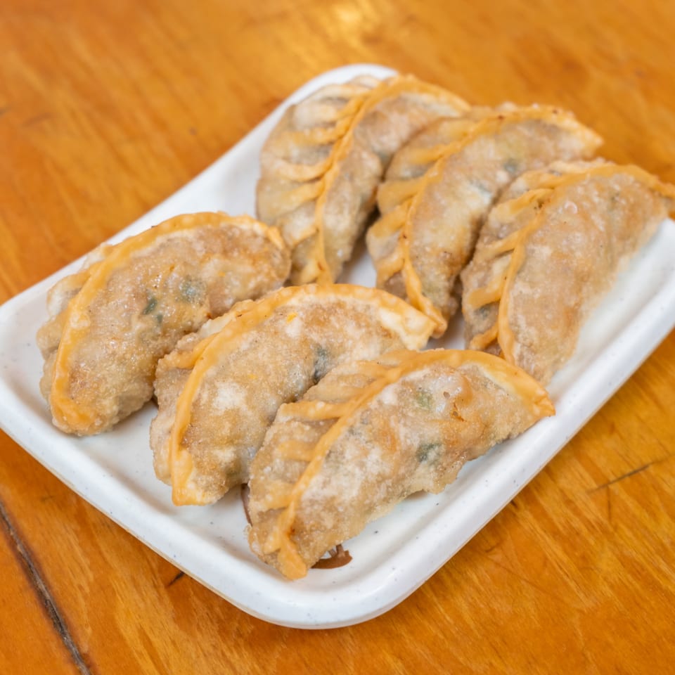 A plate of golden fried dumplings arranged on a white dish atop a wooden restaurant table.